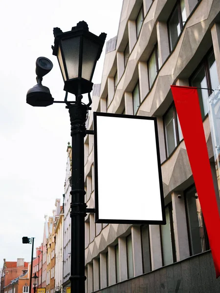 Vista laterale del cartello di bianco vuoto modello fino segnaletica in cornice nera con vecchio muro della città display di sfondo esterno. Stile moderno con decorazione artistica in metallo fabbro su lampione cittadino — Foto Stock