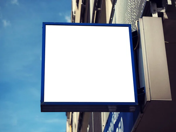 Jelzőtábla oldalnézetből üres fehér kigúnyolják jelzések kék keretben a modern fal háttér kijelző külső. Fényes égbolt nézet — Stock Fotó