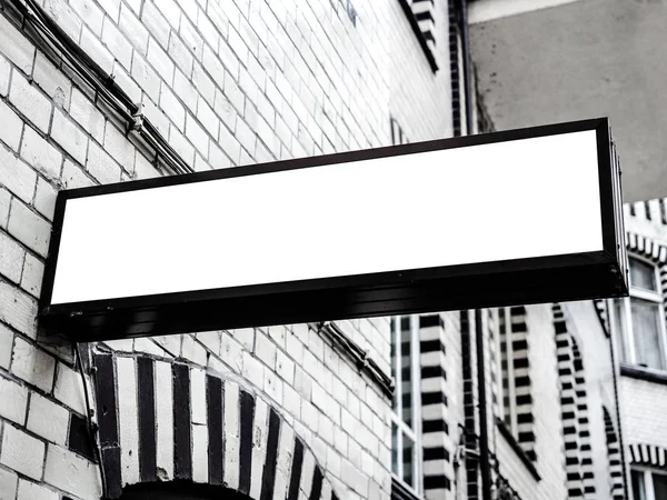 Горизонтальная белая вывеска с черной рамкой на городской стене с белым кирпичом — стоковое фото