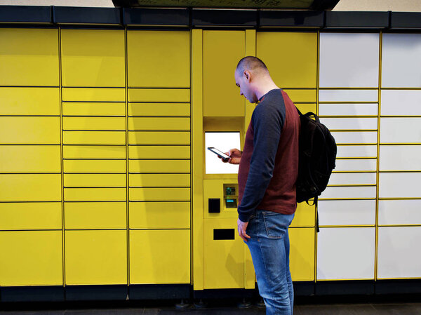 Closeup of business man hand using Electronic Locker, Yellow automated parcel terminal (parcel locker, post terminal, E-Locker) on the street with empty screen for mockup, home delivery.