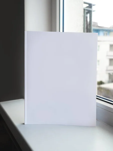 Pencerenin yanındaki beyaz masada boş boş beyaz dergi kitabı, tasarım kapağı veya şirket profili portföyü için. — Stok fotoğraf