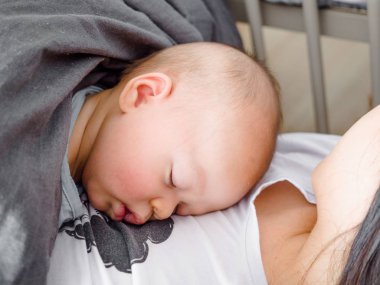 Güzel genç annenin yan görünümü yatakta uyuyan bebeği bebek oğlu tutuyor, karışık yarış yarı Asya Kafkas 3 ay eski