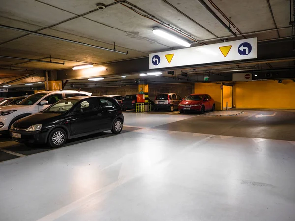 Många parkerade bilar i ett parkeringshus i köp centret, upplyst underjordisk bil parkering interiör under modern galleria med massor av fordon och pilar på golvet — Stockfoto