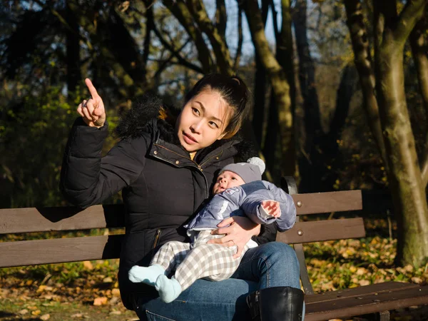 Happy Asian young mother walking with baby outdoors in the park during Autumn, good cold weather, happy child, mixed race family, half Asian Half European. Autumn scene of mother kissing young baby