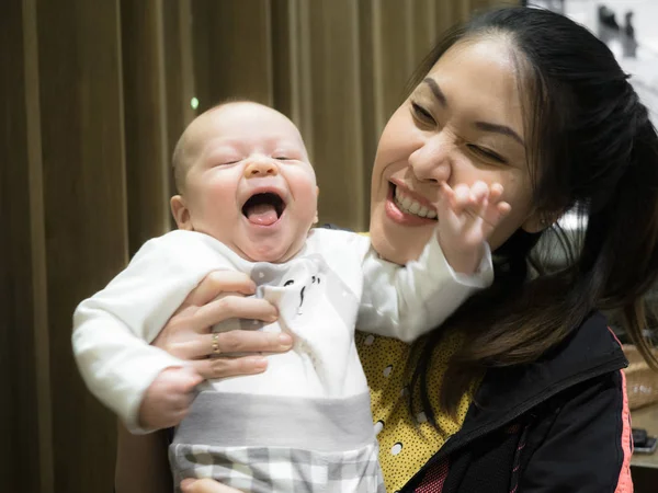 Happy Asian young mother sitting in the restaurant, talking, happy child, mixed race family, half Asian Half European. Infant baby, young family