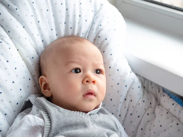 Cute 4 months old mixed half race Asian Caucasian boy looking happy smiling and laughing at the camera, healthy child baby boy. Half Thai half Polish. Winter, elegance cloth sitting next to window