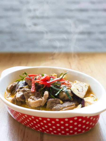 Delikátní domácí koření thajské jídlo se zeleninou, vepřovým masem a kuřecím kořeněným kari v červených bodech hluboké desky na dřevěném stole. — Stock fotografie