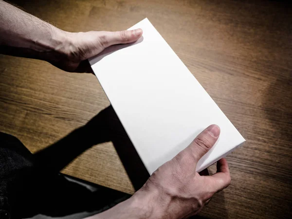 Мужчина (мужчина) двумя руками держит пустую (пустую, вакантную) бумажную коробку, макет белый ящик, вид сбоку . — стоковое фото