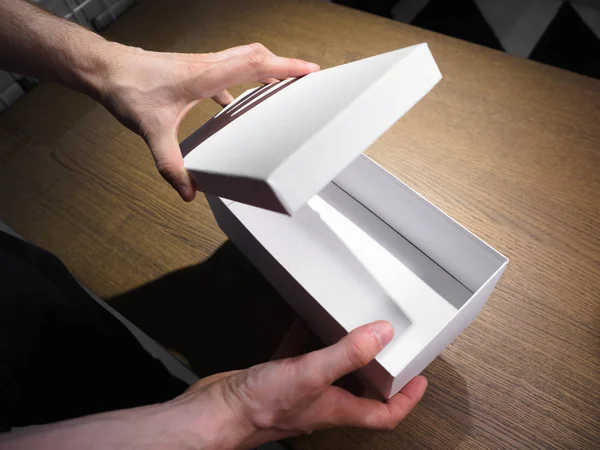 Un hombre (masculino) de dos manos sostiene y abre una caja de papel vacía (en blanco, vacante), maqueta de caja blanca, vista lateral . —  Fotos de Stock