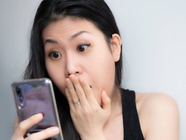 Heyecanlı genç Asyalı güzel kadın inanılmaz alışveriş mobil app satış mesaj smartphone vasıl, holding, cep telefonu arıyorum euphoric kız kazanan arıyorsunuz tarafından hayran. Büyük gözleri ile kopya alan arka plan