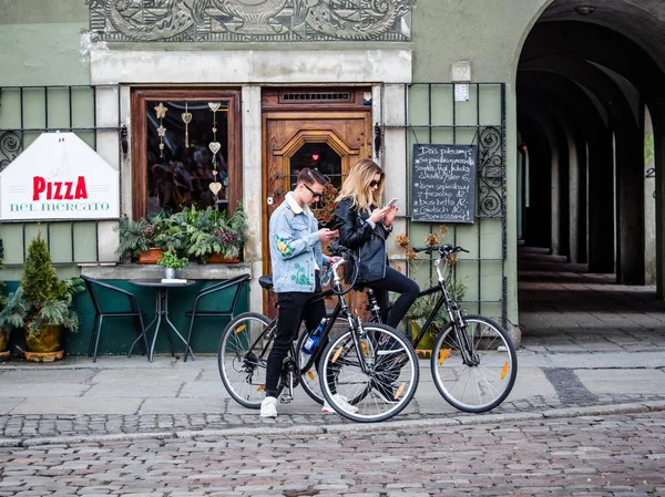 Ciudad vieja, Poznan, Polonia, 2 de abril de 2018, Jóvenes adolescentes hipster de moda hermosa, parejas, amigos, utilizando el mapa de navegación en el teléfono celular móvil, buscando en bicicleta cómo ir al lugar . — Foto de Stock