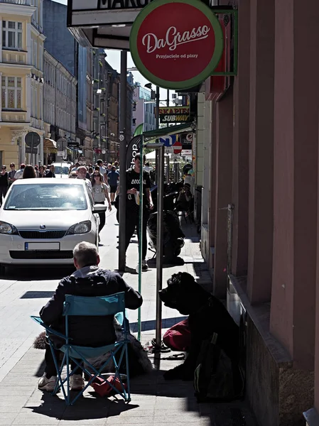 Poznan, Polonia, 3 de junio de 2017. Un pobre viejo mendigo está sentado y esperando dinero con su gran perro en una ciudad con mucha gente . — Foto de Stock