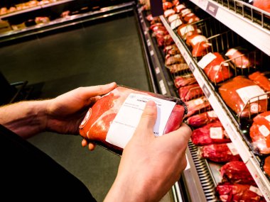 Adam et, sığır eti, domuz kalite, karşılaştırmak için nutritions bulanık ürünleri arka plan, Poznan, Polonya, 4 Nisan 2018 ile taze süpermarket raf içinde paketleri tutan eller