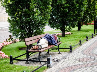 14 Nisan 2018, Poznan, Polonya, evsiz bir kişi bir ceket ile kendini kapsar ve parkta bir bankta uyuyor.