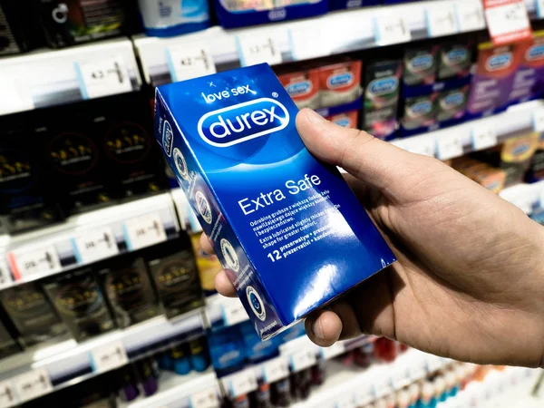 Man hands holding condom to compare and check quality the supermarket, store shelf with blurred products background, Poznan, Poland, 3 April 2018 — Stock Photo, Image