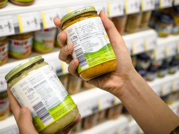 Kalite, malzemeler, bulanık ürünleri arka plan, Poznan, Polonya, 4 Şubat 2018 süpermarkette nutritions karşılaştırmak için bebek gıda kavanoz holding genç kadın eller
