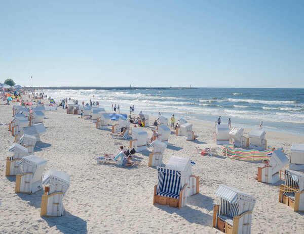 Плетеные крытые пляжные стулья на берегу моря, Балтийский пляж, полный людей в Колобжеге, Польша 16 июля 2017 г.
.