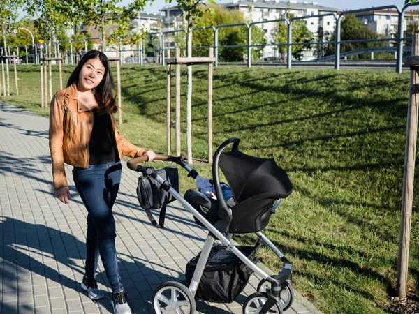 Happy young mother walking with baby stroller cart outdoors in the city, walking path