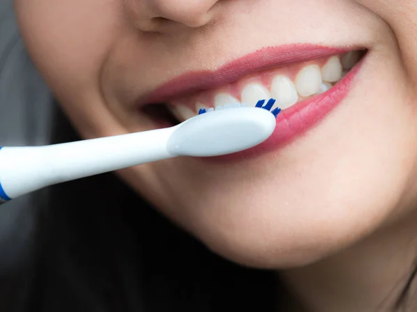 Genel bir beyaz elektrikli diş fırçası oral hijyen, sağlık ve diş hekimliği kavramında dişlerini fırçalamayı kullanan kadın oldukça hızlı elektronik diş fırçası hareketli ve ağız, sağlıklı gülümseyen Temizleme.