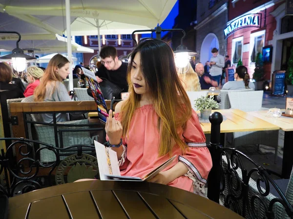 Browaria restaurante, Poznan, Polonia, Una hermosa chica asiática mirando el menú de comida, ordenando el menú en el restaurante y decidiendo qué comer, 13 Abril 2018 — Foto de Stock