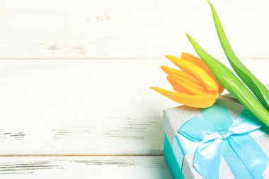 beyaz ahşap arka plan üzerinde turkuaz hediye kutusu üzerinde tebrik kartı sarı laleler. İskandinav stili, metin yeri.