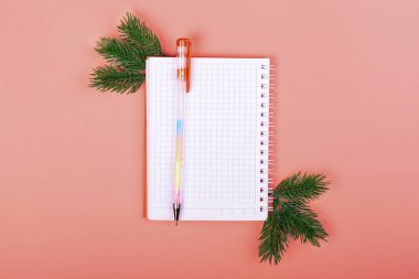 Pembe Noel arkaplanı. Noel harcamalarını kaydetmek için bir defter. Bir kalem. İki ladin dalı..