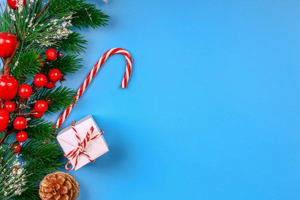Noel arkaplanı. Hediye kutusu. Firavun dalı ve konisi. Kırmızı çilek. Lolipop. Mavi arka plan. Üst Manzara. Yakın plan..
