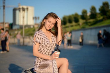 elinde kahve ile güzel kız sokakta bir bankta oturur