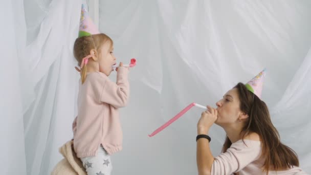 Little blondy girl and her mother blows festive horns — Stock Video