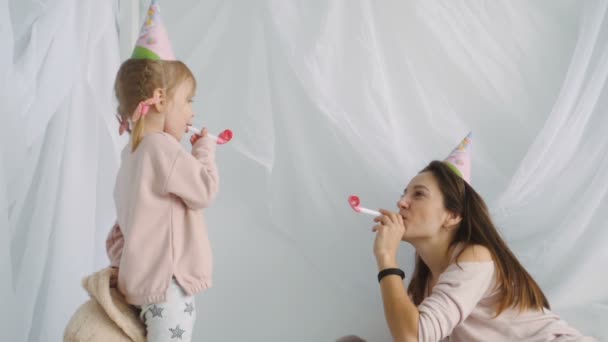 Pequeña chica rubia y su madre sopla cuernos festivos — Vídeo de stock
