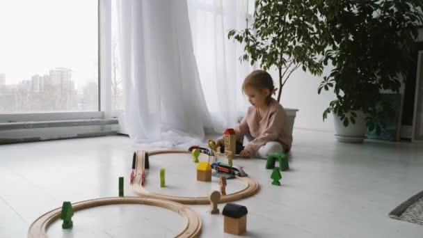 Маленькая милая дочь играет с деревянной железной дорогой — стоковое видео