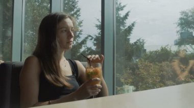 Pencere ve içecekler kokteyl yakınında oturan genç kadın