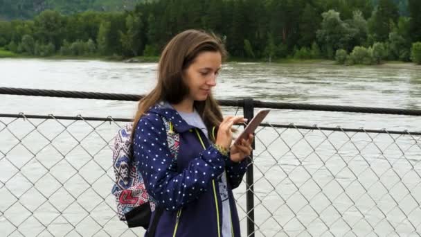 Beautiful young girl use mobile phone on the bridge — Stock Video