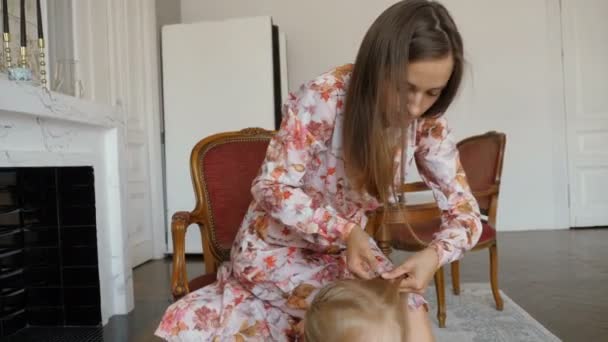 Een mooie vrouw plaits de vlecht van haar dochtertje. — Stockvideo