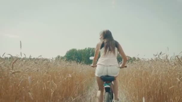 Молодая женщина ездит на велосипеде по пшеничному полю — стоковое видео