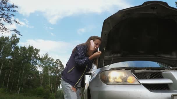 Νεαρή γυναίκα που μιλάει στο τηλέφωνο κοντά στο καπό του ένα σπασμένο αυτοκίνητο. — Αρχείο Βίντεο