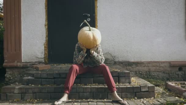 Upset pumpkin-head female sitting on the porch of an old house — Stock Video