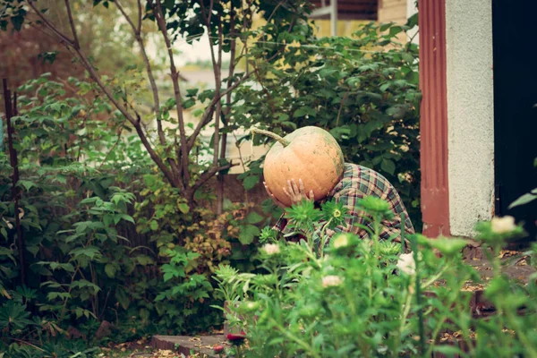Portrait of sad pumpkin-head female sitting on the porch of an old house. Disappointed person with pumpkin instead of a head