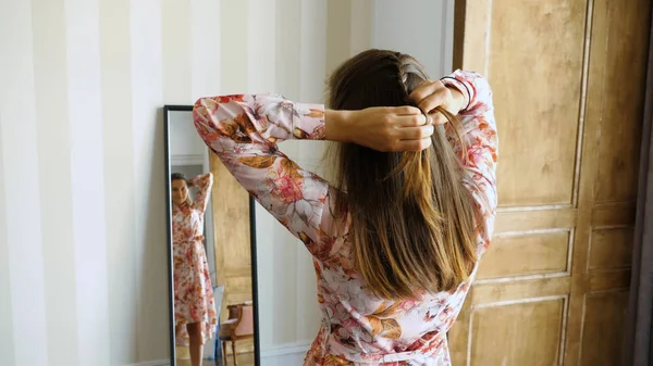 Девушка заплетает косички перед зеркалом — стоковое фото