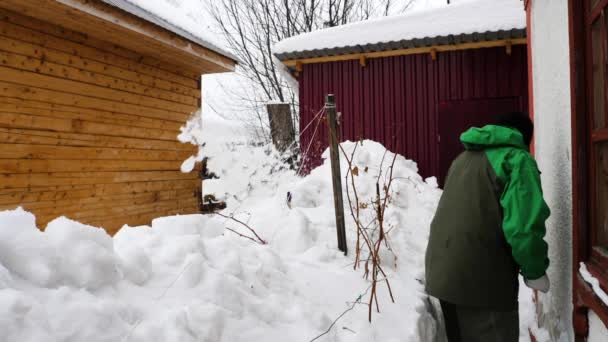 El hombre limpia la nieve cerca de la casa — Vídeo de stock
