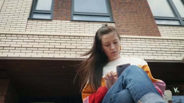 Genç ve güzel bir kadın tuğla binanın yanında akıllı telefon kullanıyor. — Stok video