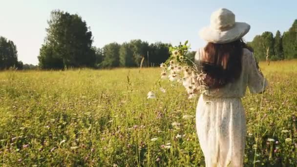 Жінка з квітами гуляє на лузі — стокове відео