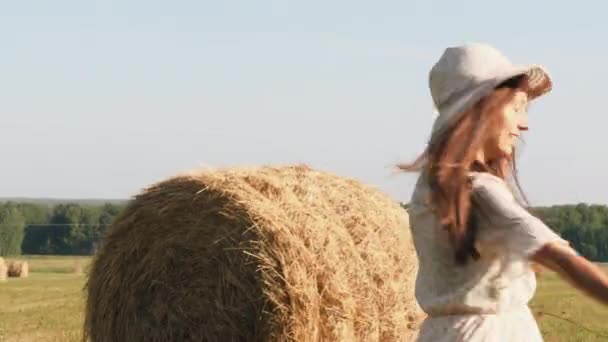 Young woman in straw hat with flowers is spinning round in the meadow — Stock Video