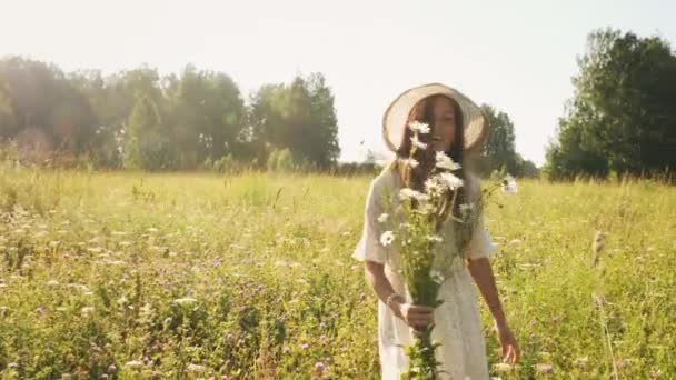 Fröhliche Frau mit Strohhut und Blumen auf der Wiese — Stockvideo