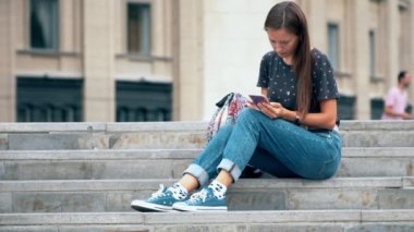 Üniversitenin merdivenlerinde oturan ve akıllı telefon kullanan öğrenci