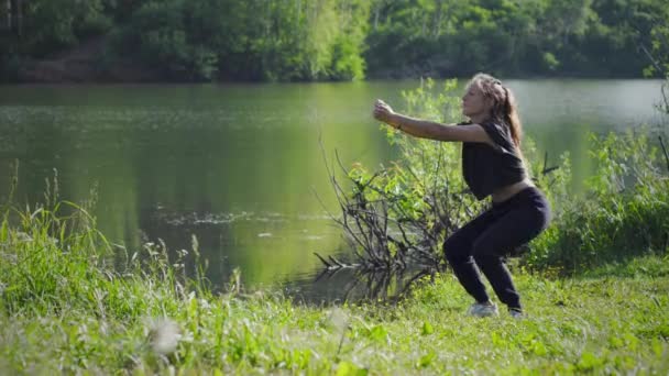 Woman makes squats on lake shore — Stock Video