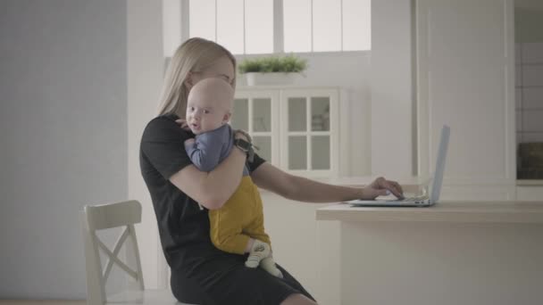 Η μητέρα εργάζεται στο σπίτι αγκαλιάζοντας το μικρό παιδί — Αρχείο Βίντεο