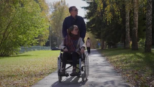 Женщина в инвалидной коляске с парнем в осеннем парке — стоковое видео