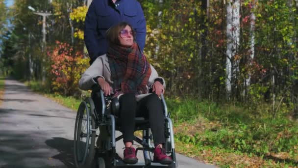 Мужчина ходит с женщиной в инвалидном кресле — стоковое видео