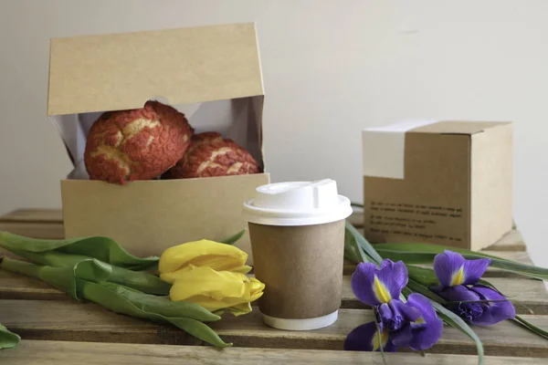 A glass of coffee, flowers tulips, a pack of coffee and cakes on a wooden table against the background of a light wall. 8 march